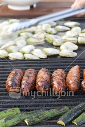 Cooking dinner of sausages and tuatua outdoors on a Barbeque, 
