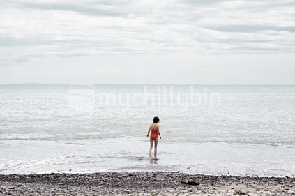 Woman getting into the cold sea for a swim on a stony beach