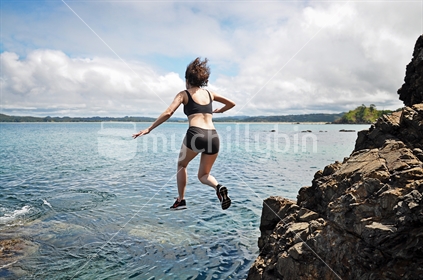 Woman jumps off high rocks into the sea (selective focus and some motion blur)