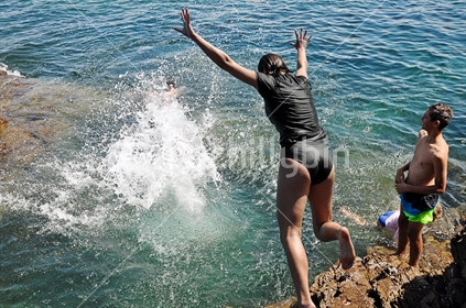 Kids jump off high rocks into the sea (selective focus and some motion blur)