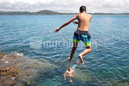 Kids jump off high rocks into the sea (selective focus and some motion blur)