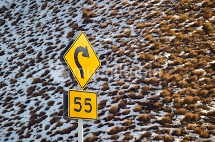 Tight curve speed sign against snowy tussock