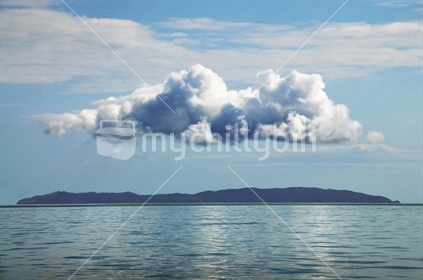 Aotearoa, Land of the Long White Cloud. A single white cloud floats above an island, and is reflected in the Sea. Hauraki Gulf, Auckland, New Zealand