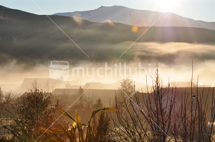 Early morning fog hangs over rooftops in a Queenstown suburb, New Zealand