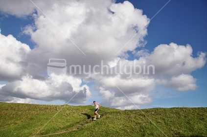 A jogger (in motion) runs down steps on a grassy hill, Mt Hobson, Auckland, New Zealand.