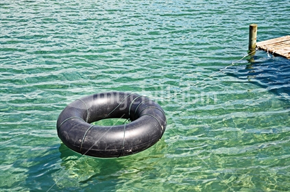 Inflated tractor inner tube tied to a jetty in the summer sun.