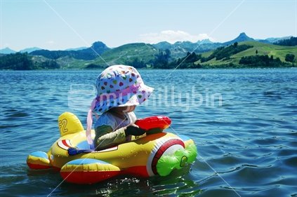 A little girl floats in an inflatable plane on Pauanui estuary on a Summer's day