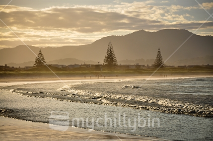 People stroll on Omaha Beach at dusk, Rodney District, North Island, New Zealand.
