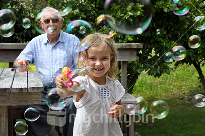 Grandfather and granddaughter blow bubbles together (selective focus and some motion blur)