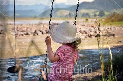 Young girl on a swing looks out on Opoutere Estuary, Coromandel, North Island, New Zealand