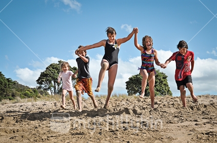 Five happy kids jump off a sand dune at the beach (see also image #100468_320)