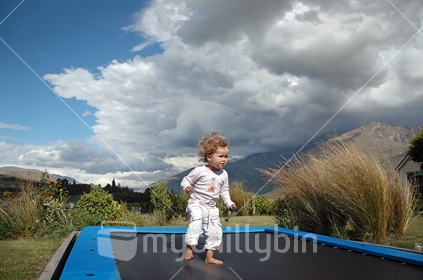 In the back yard. A young girl Struggles to trampoline in a howling Southerly gale (selective focus and some motion blur)