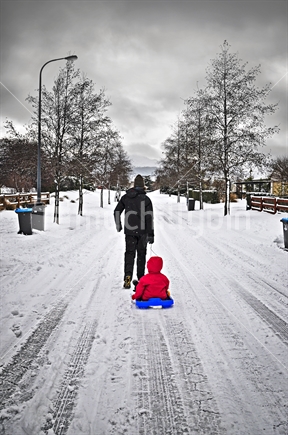 Dad pulls his daughter home on a toboggan before the storm arrives, suburban street, Queenstown, 