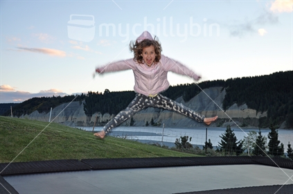 A happy young girl does a star jump on a trampoline at dusk (some motion blur) (see also #100468_467)