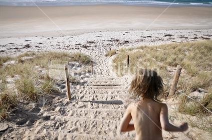 Young girl runs down an access path to a deserted beach (motion blur)