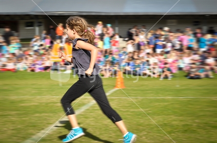 A young girl crosses the finishing line at a school cross country race (motion blur)