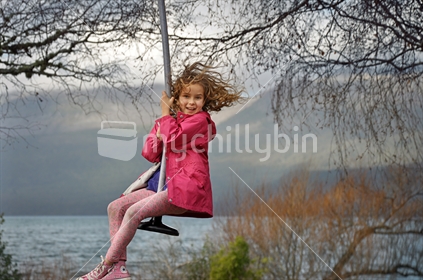 Happy girl on a swing at Lake Tarawera near Rotorua (selective focus and some motion blur)