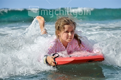Low Down Perspective: A young girl on a boogie-board in big waves at Tawharanui (selective focus)