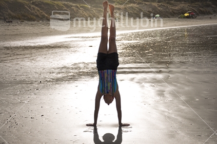 A girl does a handstand on the beach