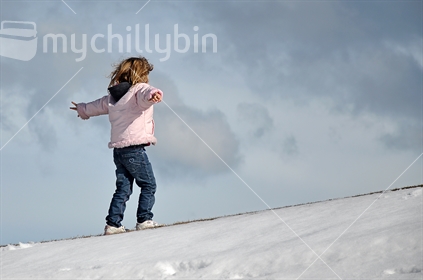 Young girl leans into the wind on a snowy hill