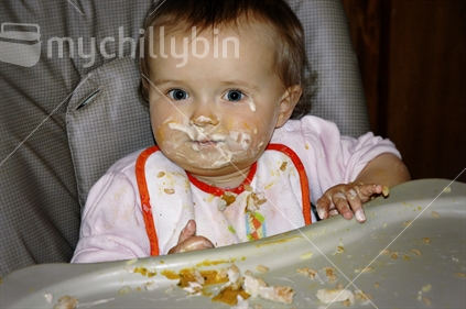 A baby girl makes a mess eating her dinner