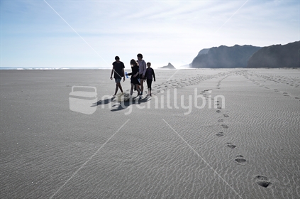 Kids walk across Karekare beach at low tide