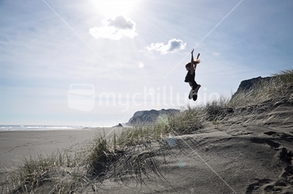 A girl leaps off the dunes at Karekare black sand beach