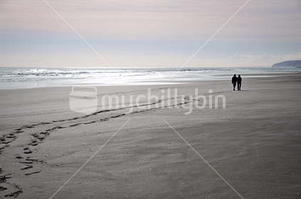 A couple walk along Karekare black sand beach at low tide