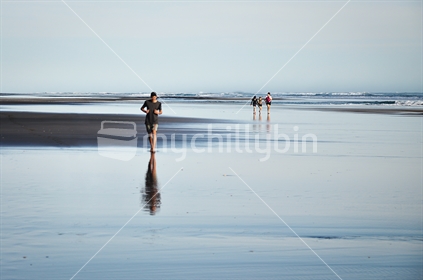 Kids walk across Karekare black sand beach at high tide 