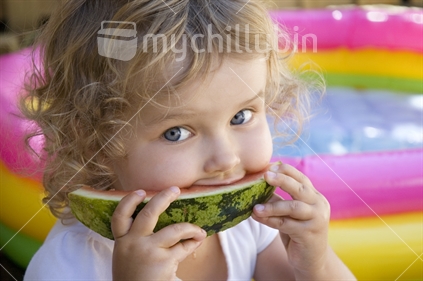 Young girl eats a watermelon - beside a paddling pool