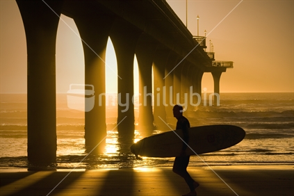A longboarder runs past the pier and off to work for the day after a surf early one morning, New Brighton, Christchurch