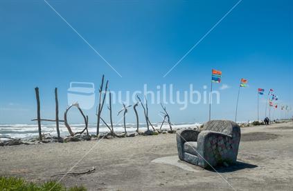 Hokitika Beach with easy chair, driftwood sign and flags.