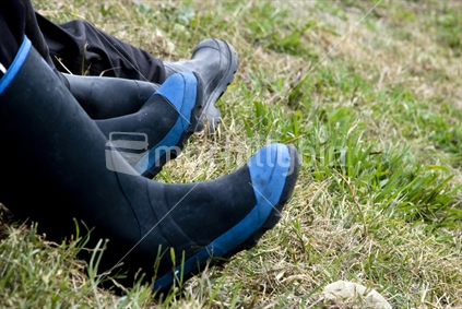 Farming gumboots being worn by people sitting on hill in paddock