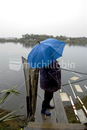 Woman standing on whitebait stand by river holding blue umbrella
