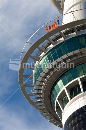 Skytower column in Auckland; with people walking on an upper outer track. 