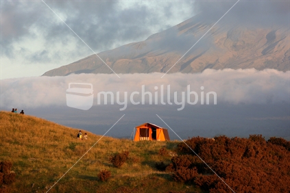 A lone tent on the side of a hill in front of Mount Taranaki
