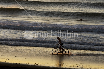 A girl riding her bike on a beach at sunset