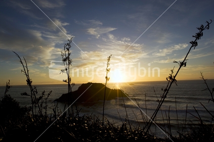 Sun setting behind an island at a west coast beach, New Zealand