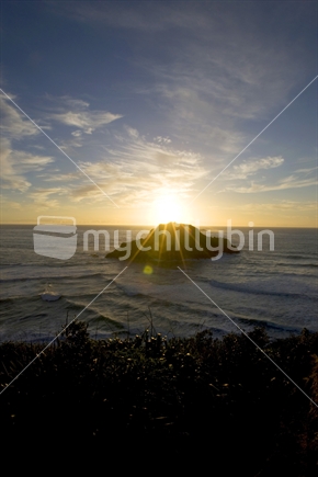 Sun setting behind an island at a west coast beach, New Zealand