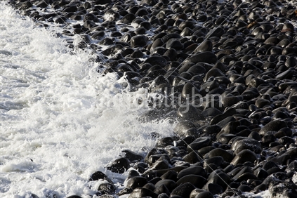 Wave crashing over rounded rocks, on the Taranaki coast, New Zealand