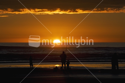 A Family playing and fishing at the beach in front of a setting sun, New Zealand