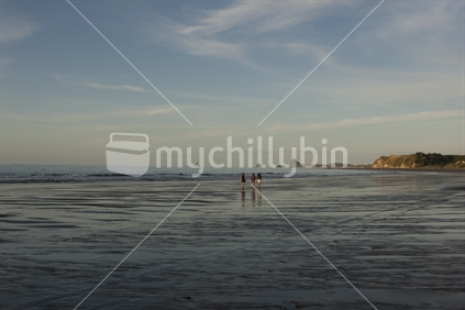 Three young people walking along a west coast beach at low tide in late evening sun, New Zealand