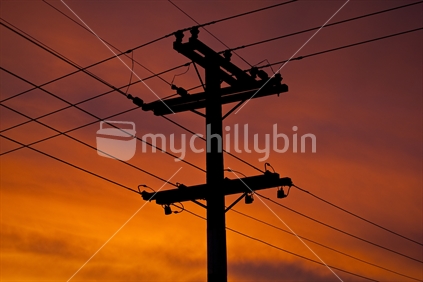 Power pole and powerlines silhouetted against a bright red sunset