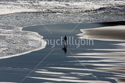 A lone surfer walking across the beach to the waves