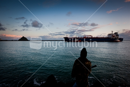 A fisherman watching a ship enter Port Taranaki, New Zealand.
