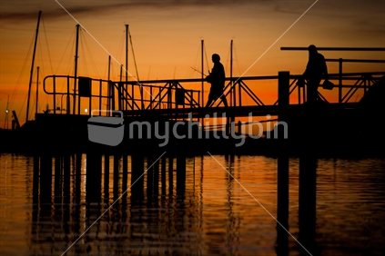 Two fishermen silhouetted by a dusk sky, on a wharf at Port Taranaki, New Zealand.