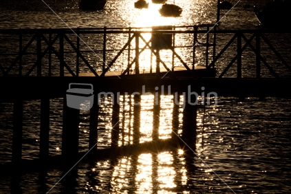 A wharf silhouetted by a setting sun sparkling in the water.