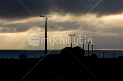 Power poles and lines on a rural road backlight by storm clouds