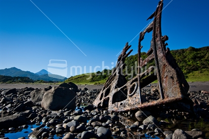 A ship wreck remains of SS Gairlock on a rocky Taranaki coastline near New Plymouth. Mt Taranaki & Kaitake ranges in the background.