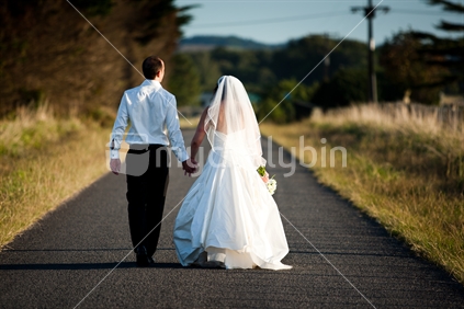 A bride & groom walking down a country road on their wedding day.
